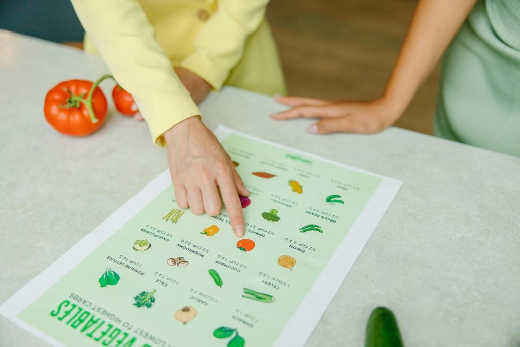 pexels photo 8844387 8844387 Close-up of hands pointing to a vegetable nutrition chart with fresh tomatoes on the table.